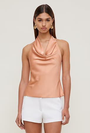Model is wearing an orange cowl neck blouse with white shorts.