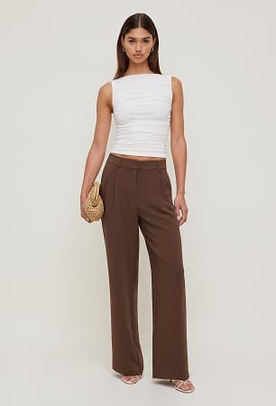 Model is wearing a white tank top with brown pants.