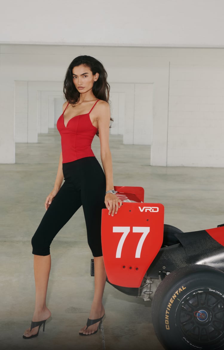 Model is wearing a red bustier camisole and black capri pants.