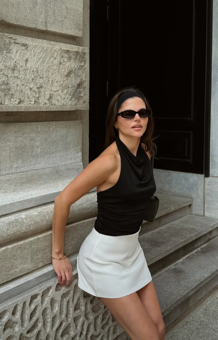 Model is wearing a black cowl neck tank top with a white mini skirt.