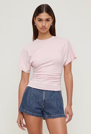 La mannequin porte un t-shirt rose et un short en denim foncé.